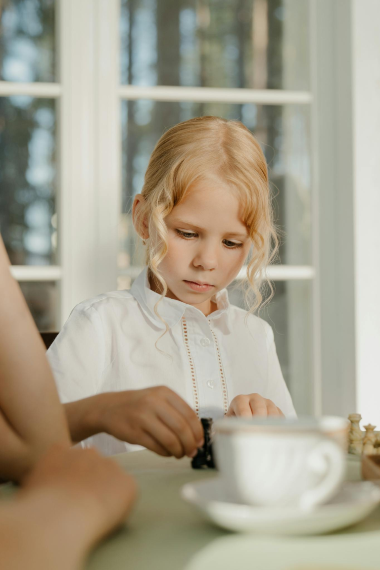 Blonde child in white shirt playing chess with focus on game pieces.